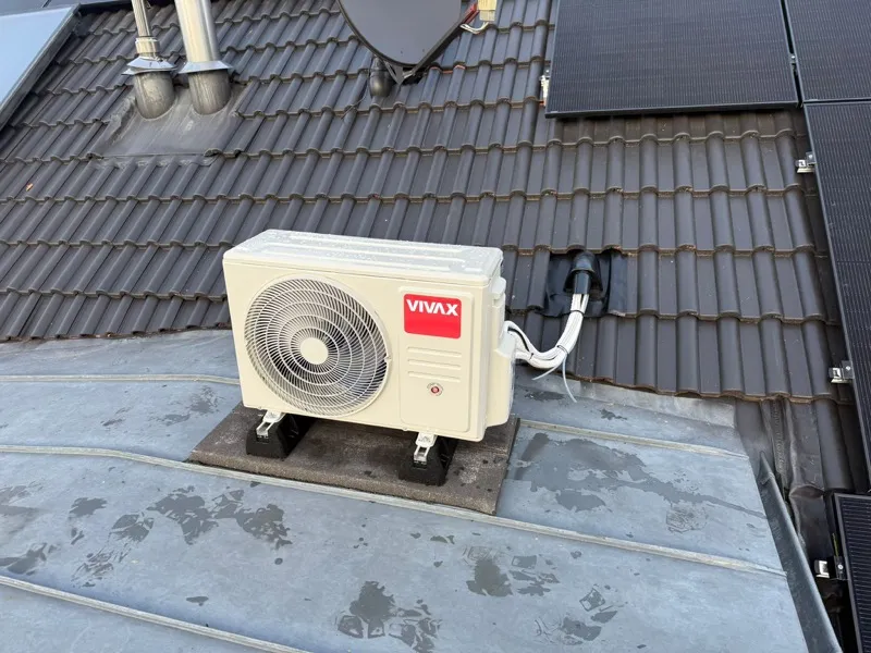 Außengerät einer Klimaanlage auf einem Dachvorsprung neben Photovoltaikmodulen